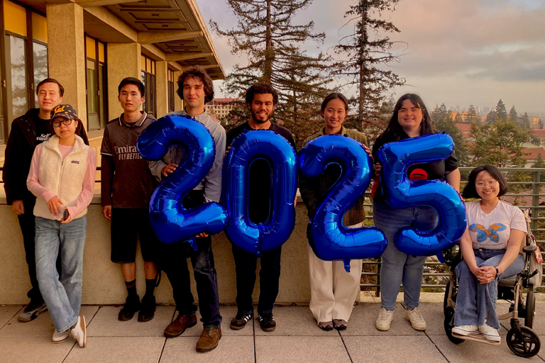 Eight Berkeley Geography students holding a 2025 balloon on a balcony