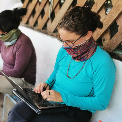 woman with glasses wearing a mask typing on laptop
