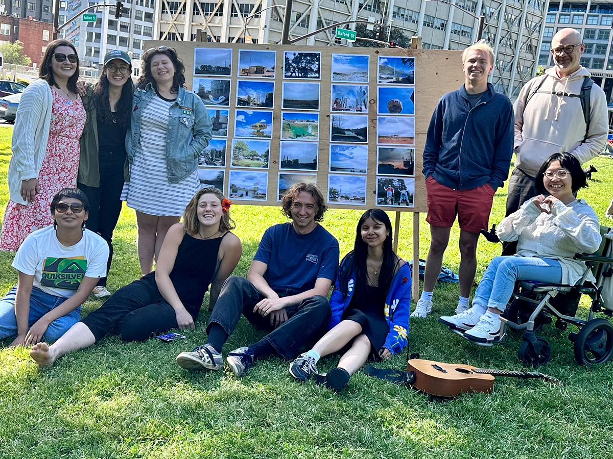 students smiling at camera standing in front of visual geographies photography exhibit