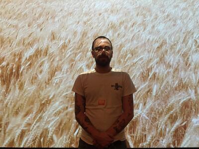 Portrait of Robert Moeller, a white man in a tee shirt standing in front of a projected image of a wheat field.